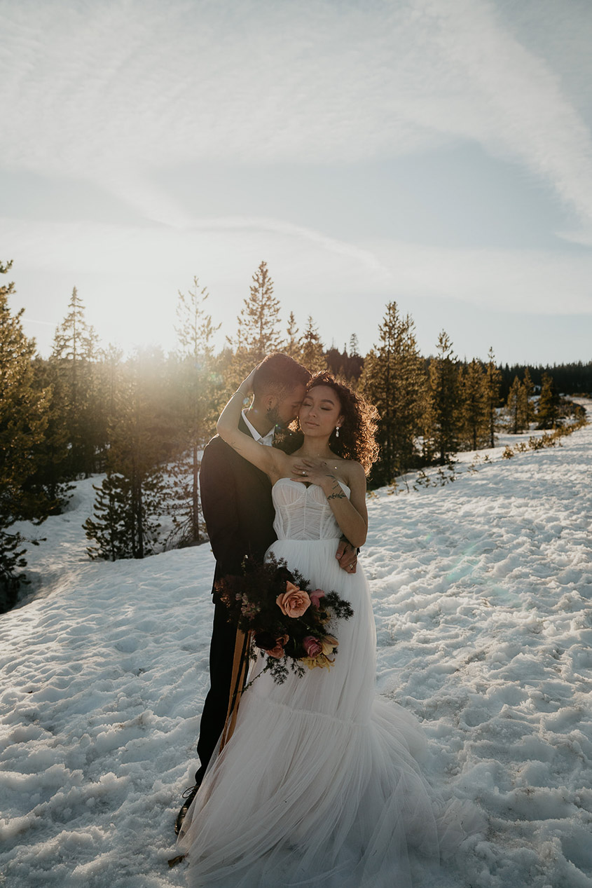 The bride and groom embracing each other in the snow. 