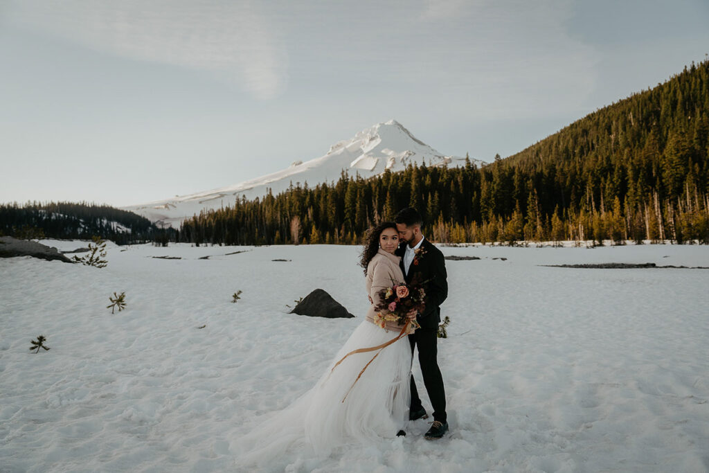 The newlyweds holding each other in the snow with Mt Hood in the background. 