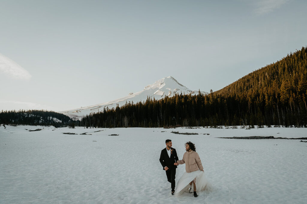 the newlyweds holding each other and walking in the snow with Mt Hood in the background.