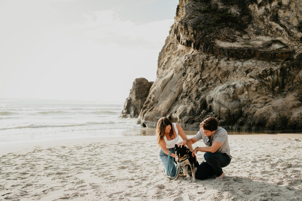 a couple bending down and petting their dog on the sand along the Oregon Coast. 