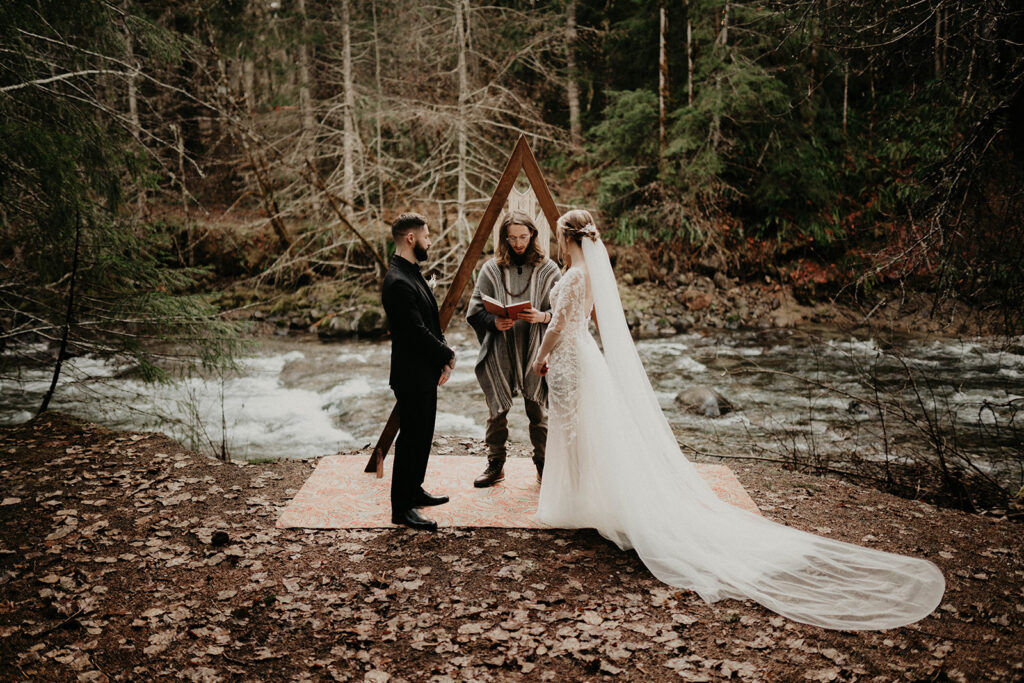 Bride and groom stand on a rug near a river during their Mount Rainier elopement in the forest