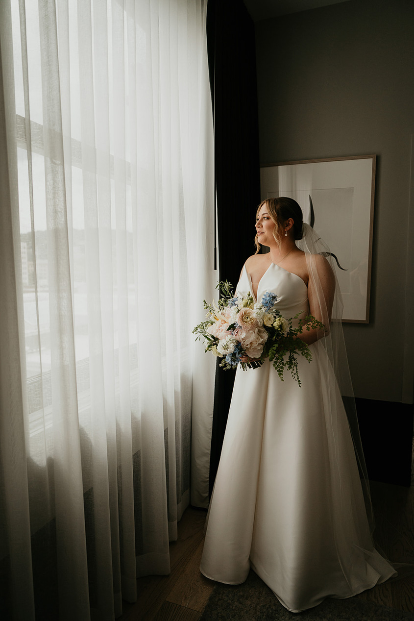 the bride looking out a window with her bouquet. 