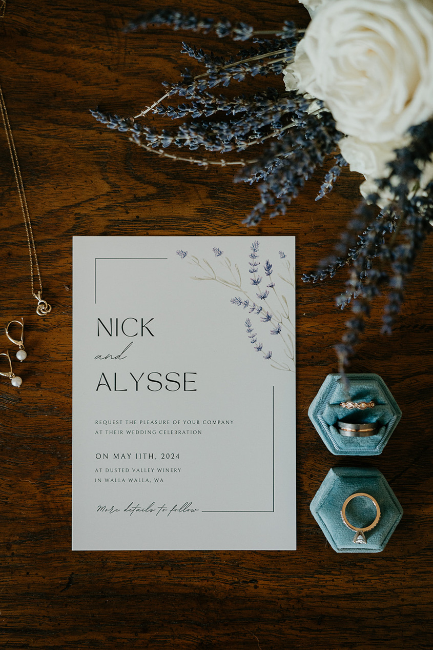 the wedding invite, earrings, necklace, wedding rings, and lavender and a white rose. 