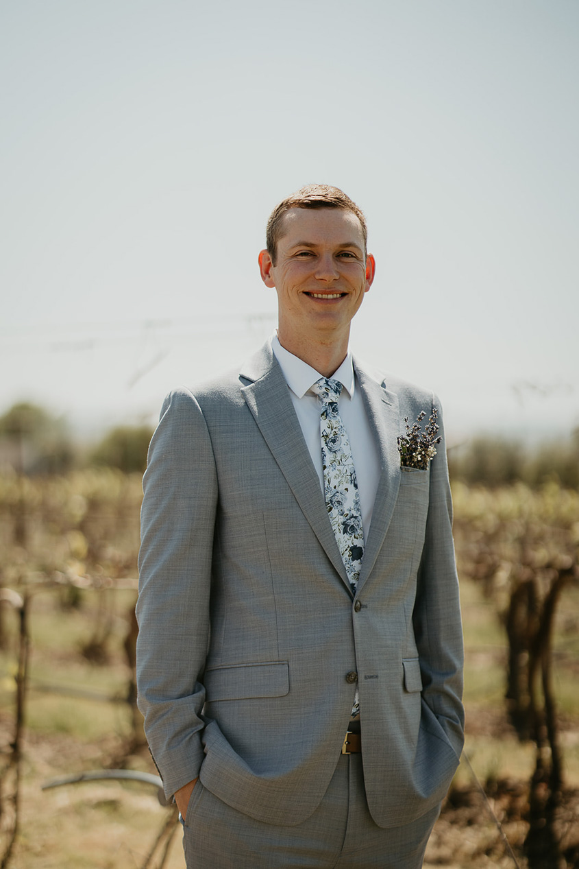 the groom smiling with grape vines in the background. 