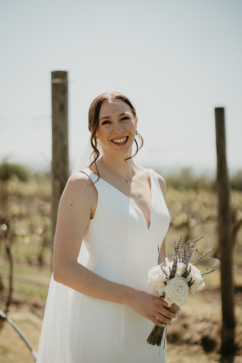 the bride posing in front of grape vines. 