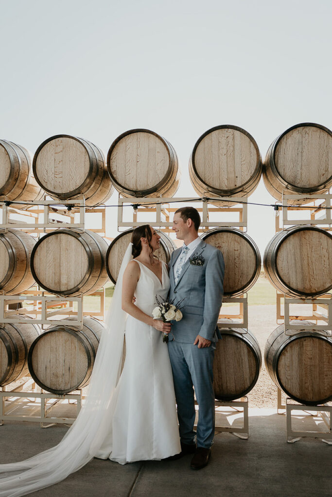 the bride and groom posing in front of wine barrels. 