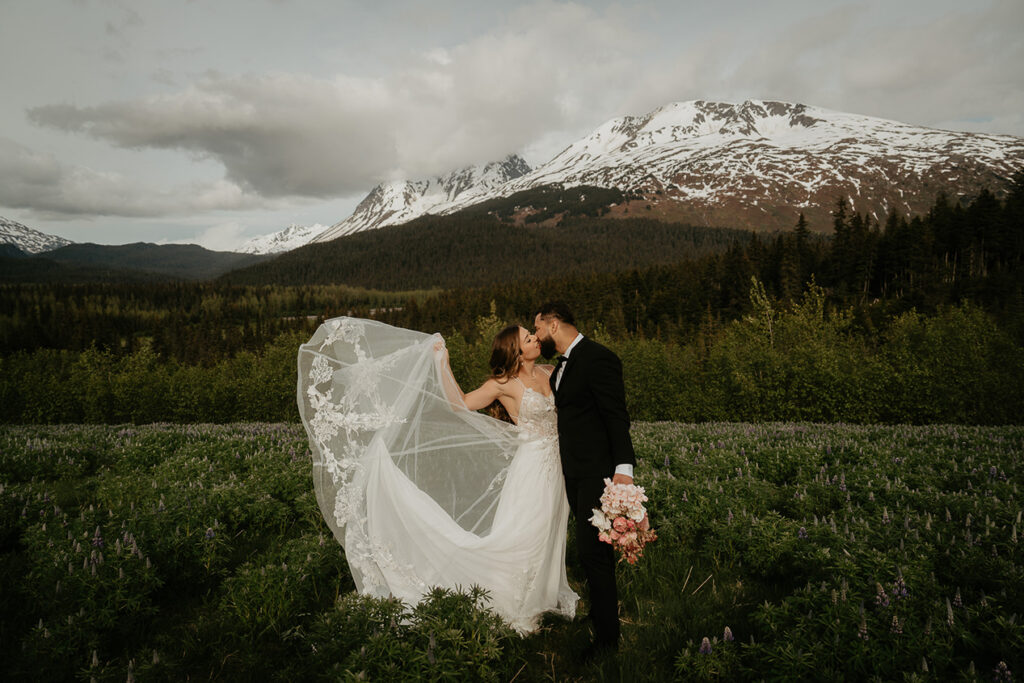 The couple kissing in a lavender field with mountains in the background while they elope in Alaska. 