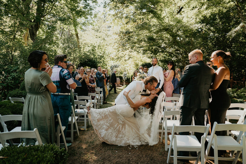 the newlyweds kissing surrounded by their wedding guests at their ceremony. 