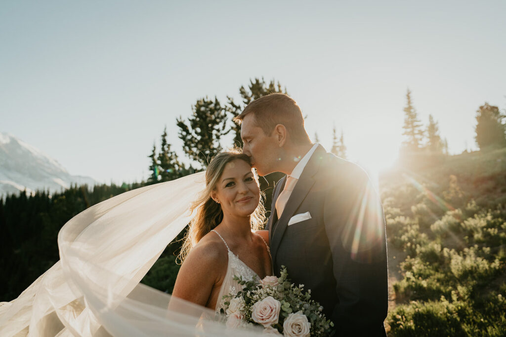 Newlyweds embracing each other while the bride's veil flows in the wind in Mt Rainier. 