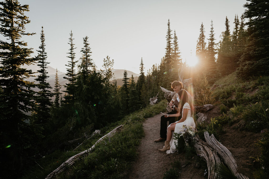 Newlyweds playing guitar at sunset on a trail. 