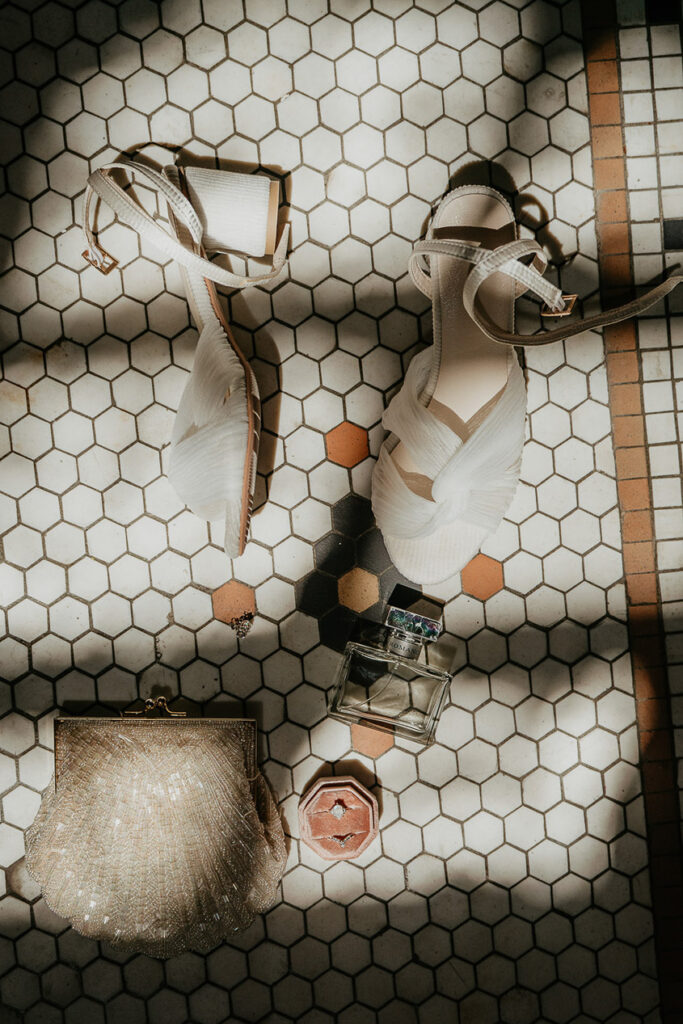 heals, perfume, purse, and wedding rings on a tile floor. 