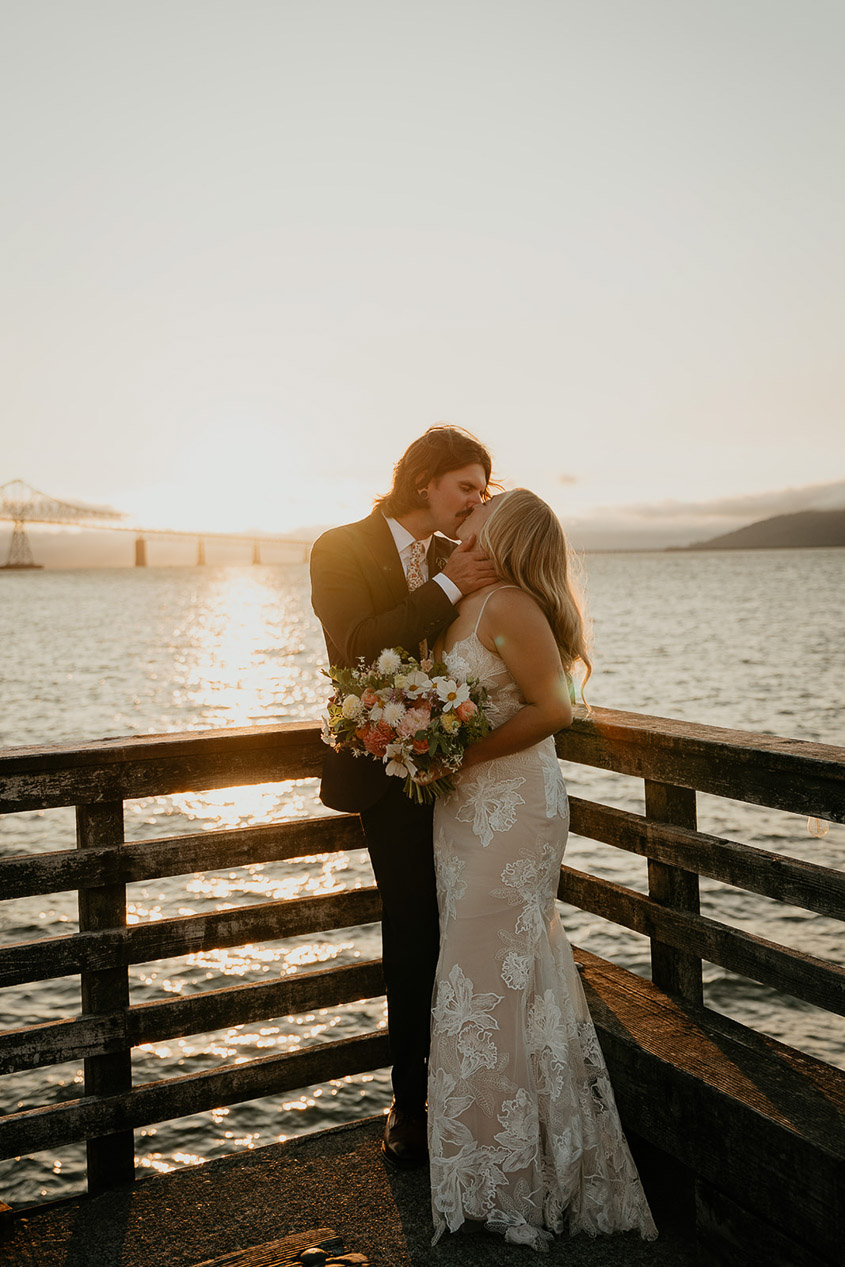 The newlyweds kissing on a dock at sunset. 