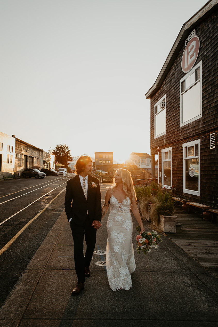 the newlyweds holding hand and walking through town at sunset. 