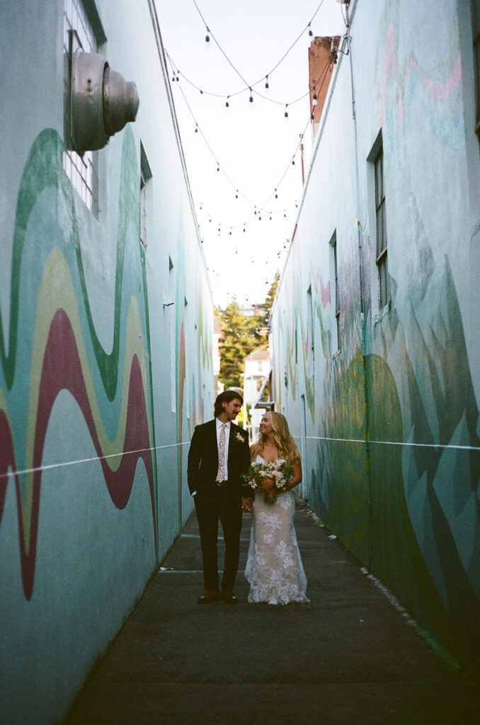 the newlyweds holding hands and smiling in an alleyway. 