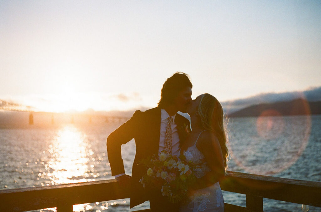 the newlyweds kissing at sunset on a dock. 