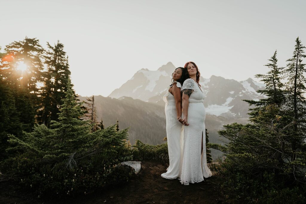 Brides hold hands while standing back to back after eloping in the North Cascades