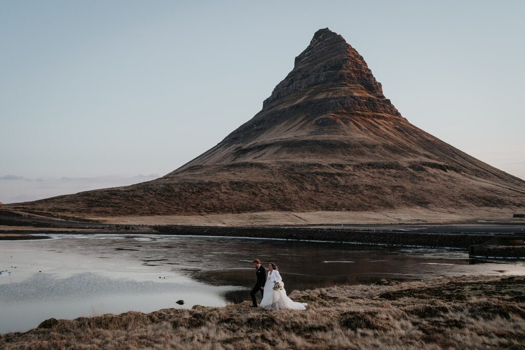 Bride and groom hold hands as they walk around Kirkjufell at their elopement in Iceland