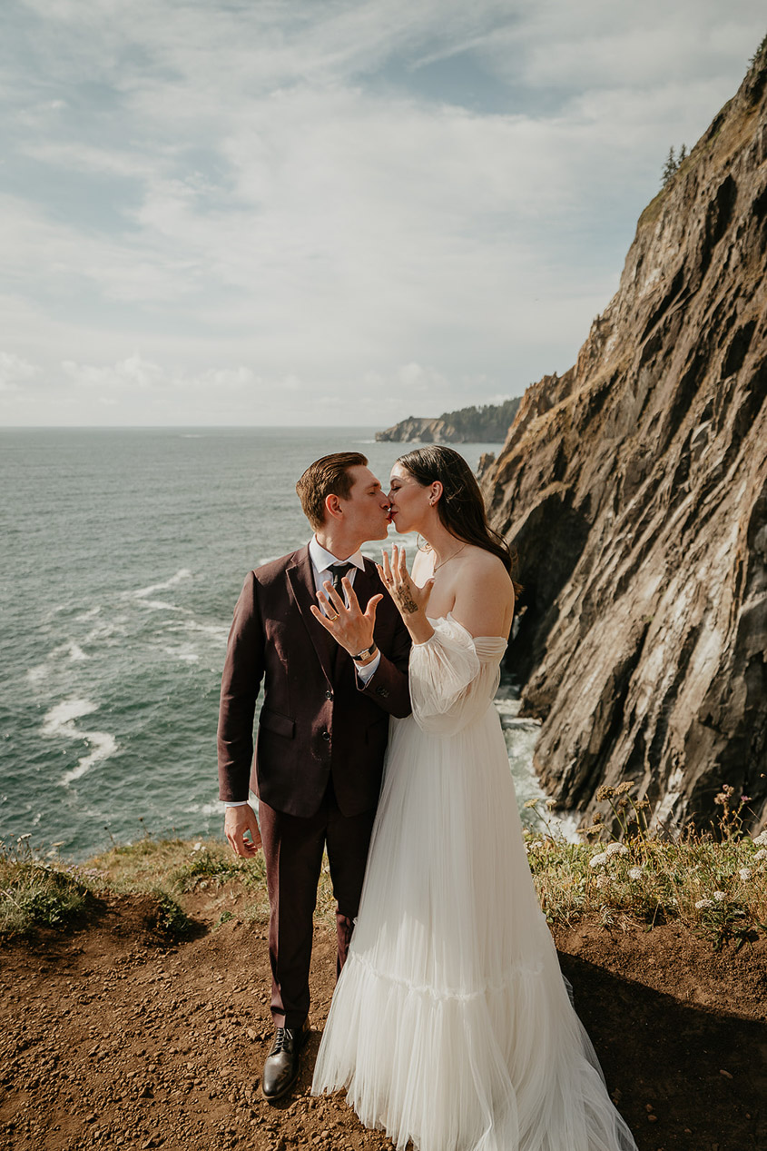 The newlyweds kissing and holding up their rings on the Oregon Coast.  