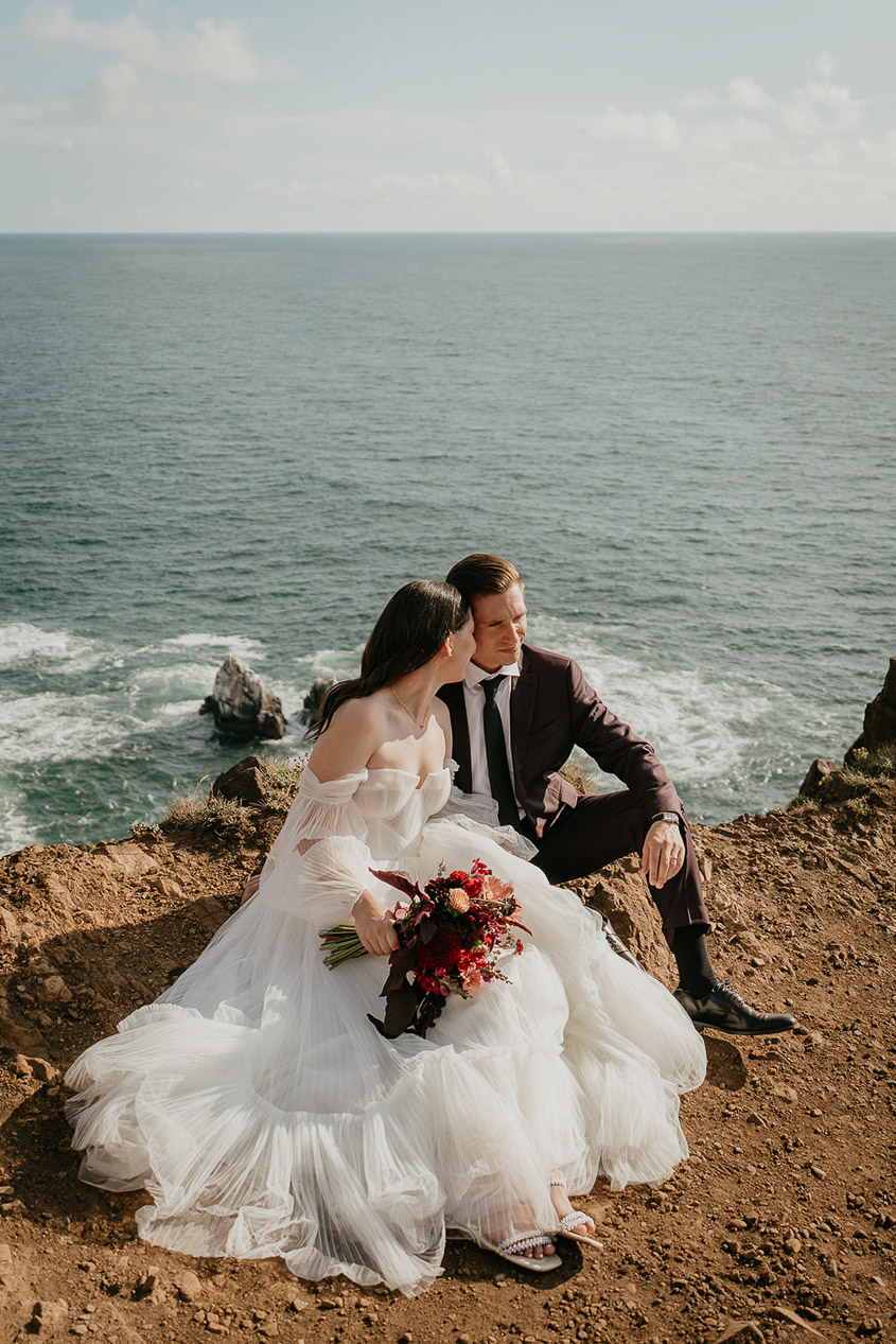 A couple sitting next to each other and holding each other during their Oregon Coast elopement. 