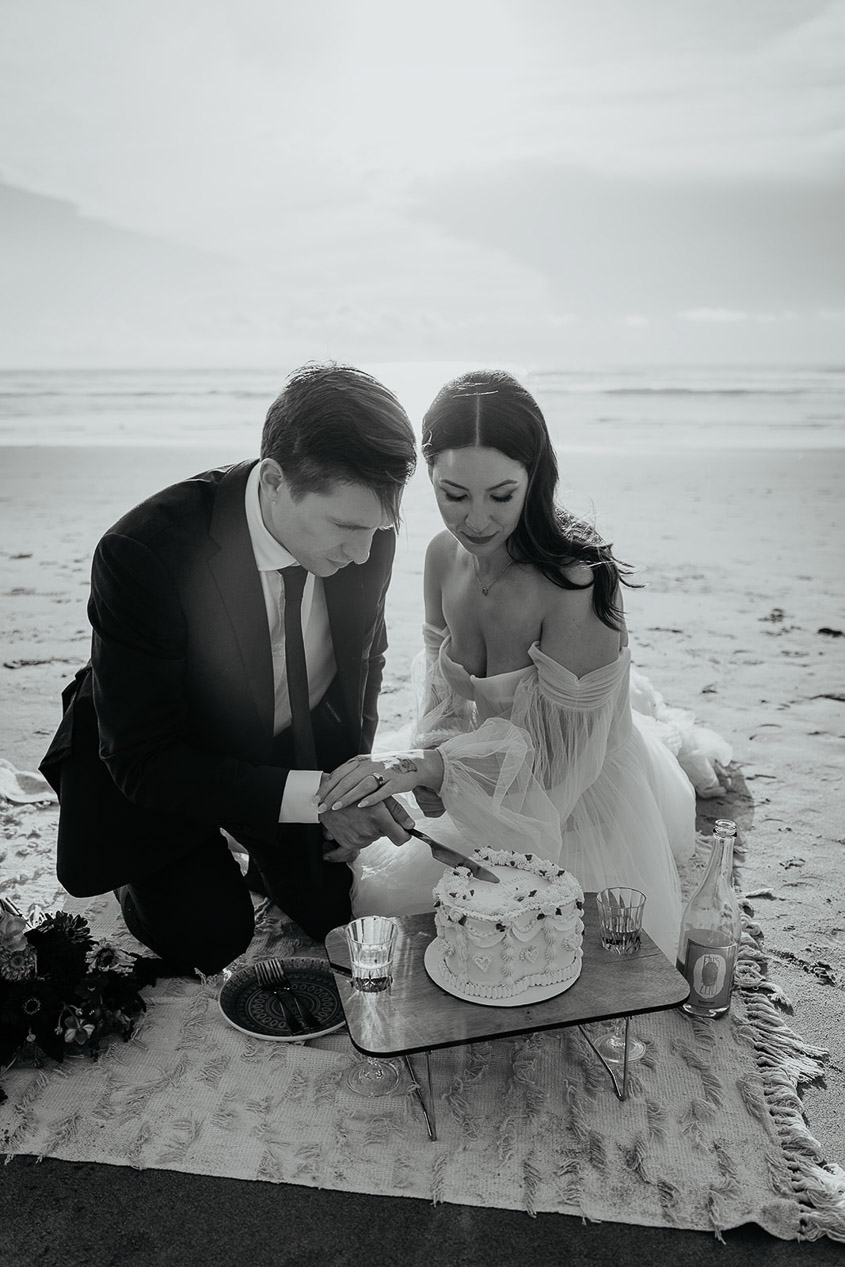 The newlyweds cutting their cake on the beach during the Oregon Coast elopement.