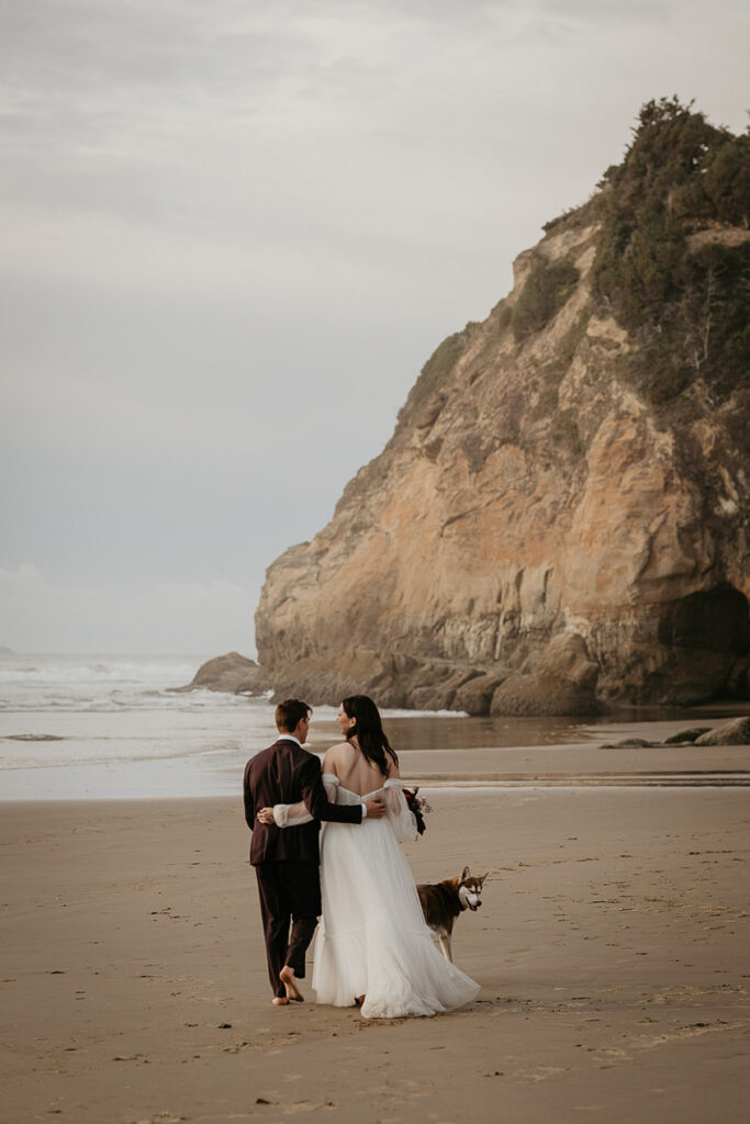 The newlyweds walking along the Oregon coast with their dog during their elopement. 