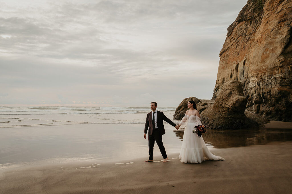 the newlyweds holding hands strolling on the beach.