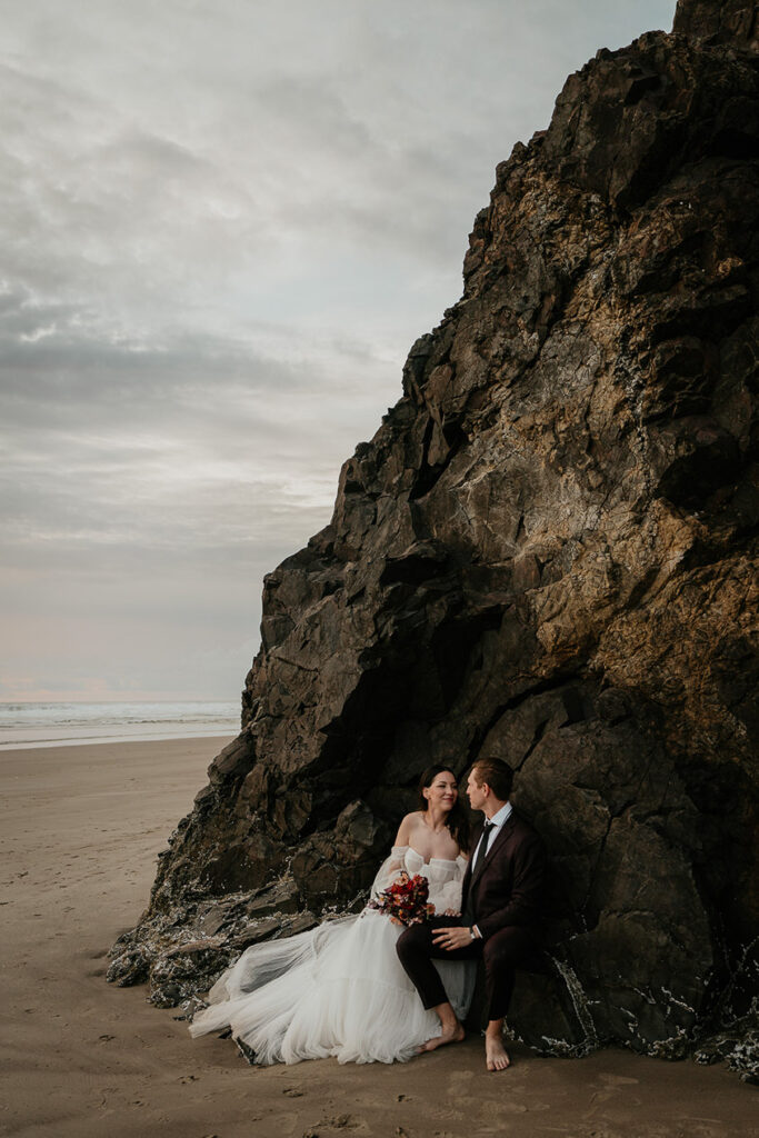 the newlyweds sitting next to a large cliff during their Oregon Coast elopement. 